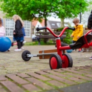 Kinderen die buiten spelen met op de voorgrond een rood loopfietsje