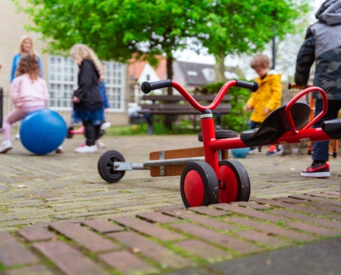 Kinderen die buiten spelen met op de voorgrond een rood loopfietsje