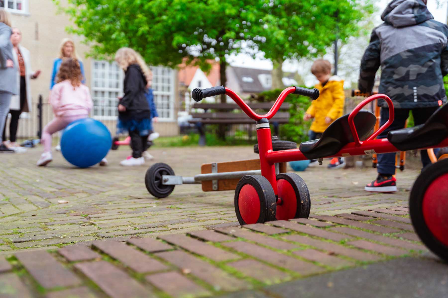 Kinderen die buiten spelen met op de voorgrond een rood loopfietsje