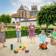 Deze kleurige foto laat het team van peuterschool De Paddestoel zien, dat buiten poseert te midden van het kinderspeelgoed.