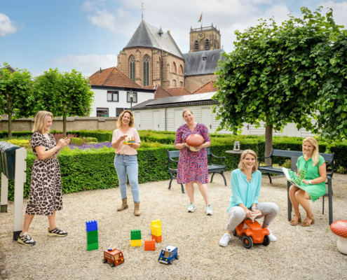Deze kleurige foto laat het team van peuterschool De Paddestoel zien, dat buiten poseert te midden van het kinderspeelgoed.